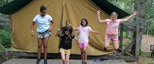 Four Girl Scouts jumping in front of a tent at summer resident camp