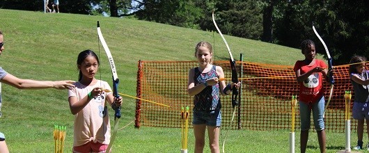 Four Girl Scouts holding bows and arrows on the archery range at camp