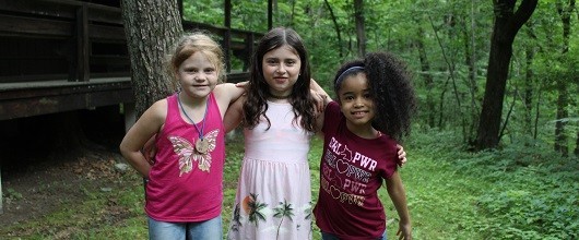 Three smiling Girl Scouts outdoors at camp