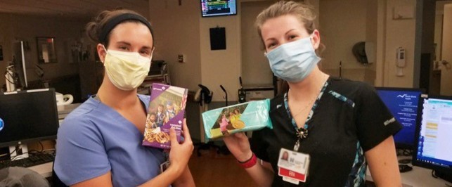 Two masked healthcare workers holding up Girl Scout Cookie boxes