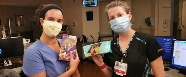 Two masked healthcare workers holding up Girl Scout Cookie boxes Two masked healthcare workers holding up Girl Scout Cookie boxes