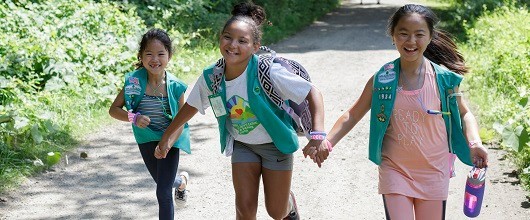 Three smiling Girl Scout Juniors running along a path outdoors