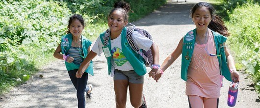 Three smiling Girl Scout Juniors running along a path outdoors Three smiling Girl Scout Juniors running along a path outdoors