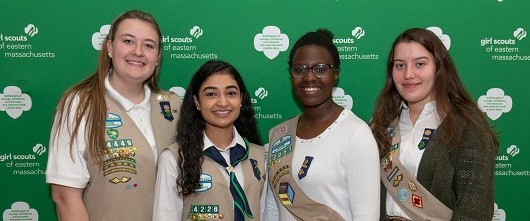 A group of four smiling GSEMA Girl Board Members standing together in front of a green GSEMA backdrop A group of four smiling GSEMA Girl Board Members standing together in front of a green GSEMA backdrop