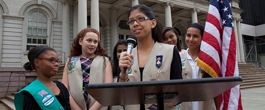 A group of Girl Scouts speaking at a podium outdoors