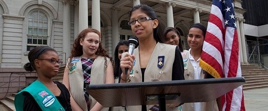 A group of Girl Scouts speaking at a podium outdoors A group of Girl Scouts speaking at a podium outdoors