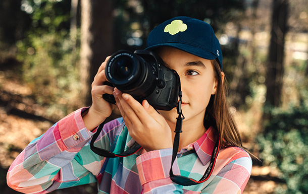 girl scout with digital camera outside wearing trefoil baseball cap