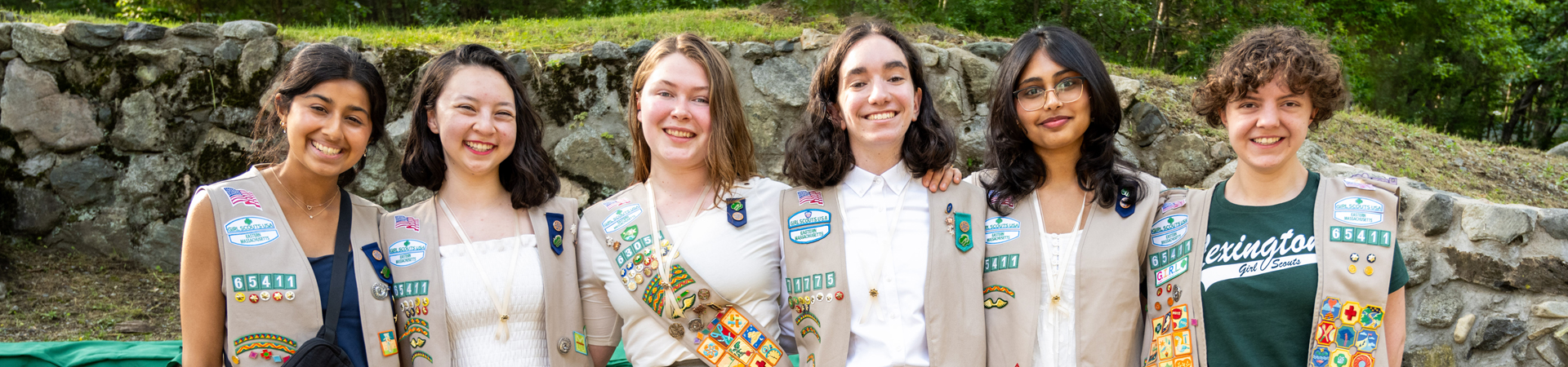  ©Ann-Marie Ford - portrait of gold award girl scouts wearing vests and smiling at camera in front of a brick building 